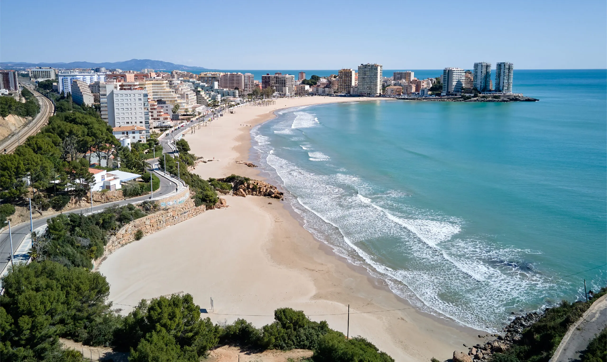 La playa de la Concha de Oropesa del Mar vista desde el pinar, con el mar en calma y el pueblo al fondo