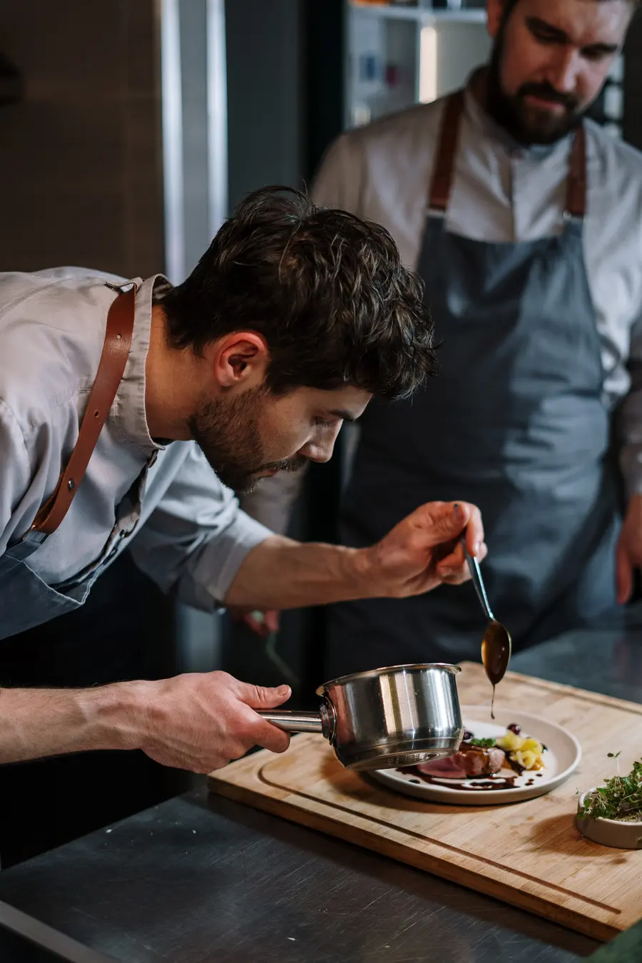 Un cocinero termina un plato con la salsa en el pase de la cocina