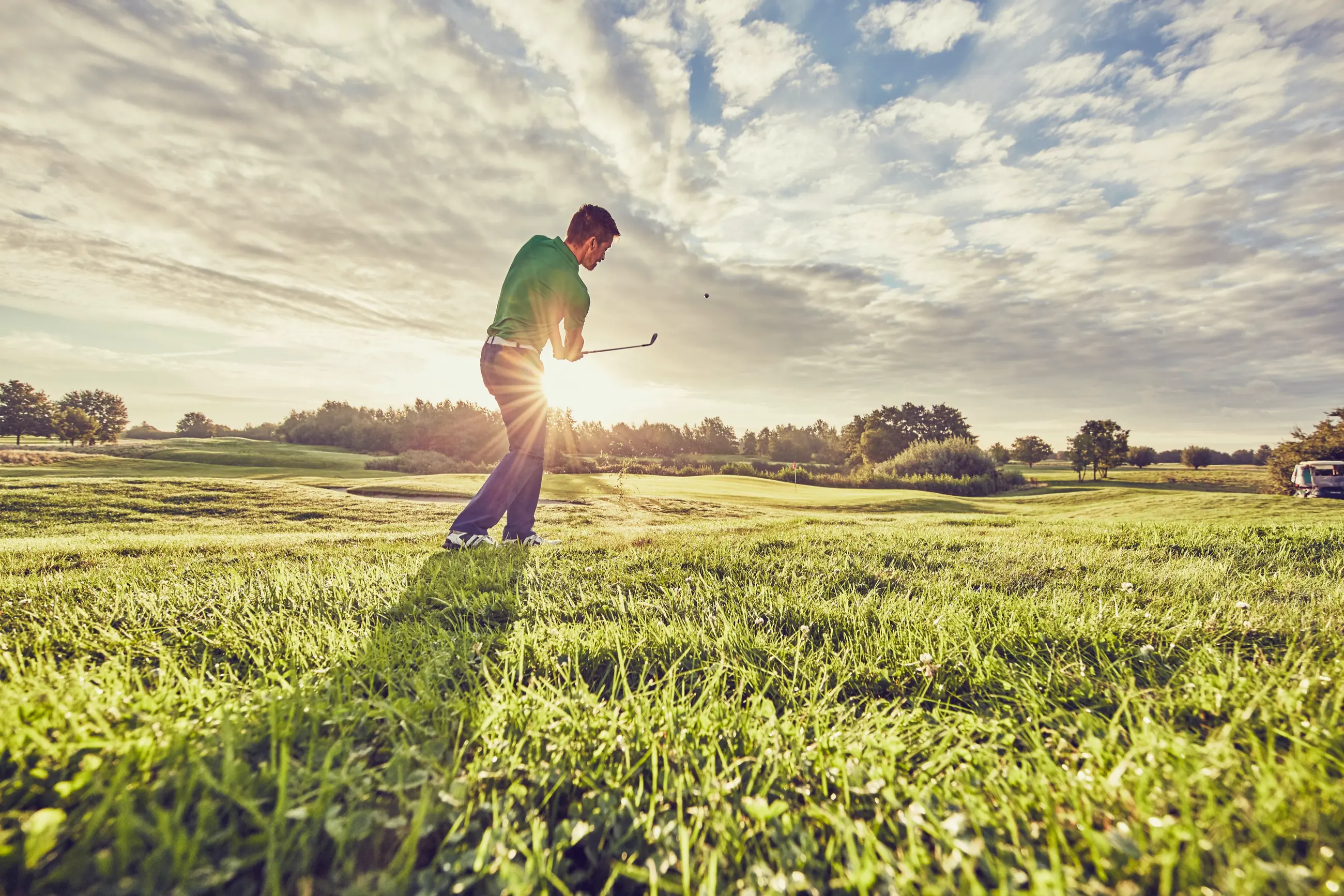 Un jugador termina el golpe en la calle de un campo de golf, a contraluz del atardecer