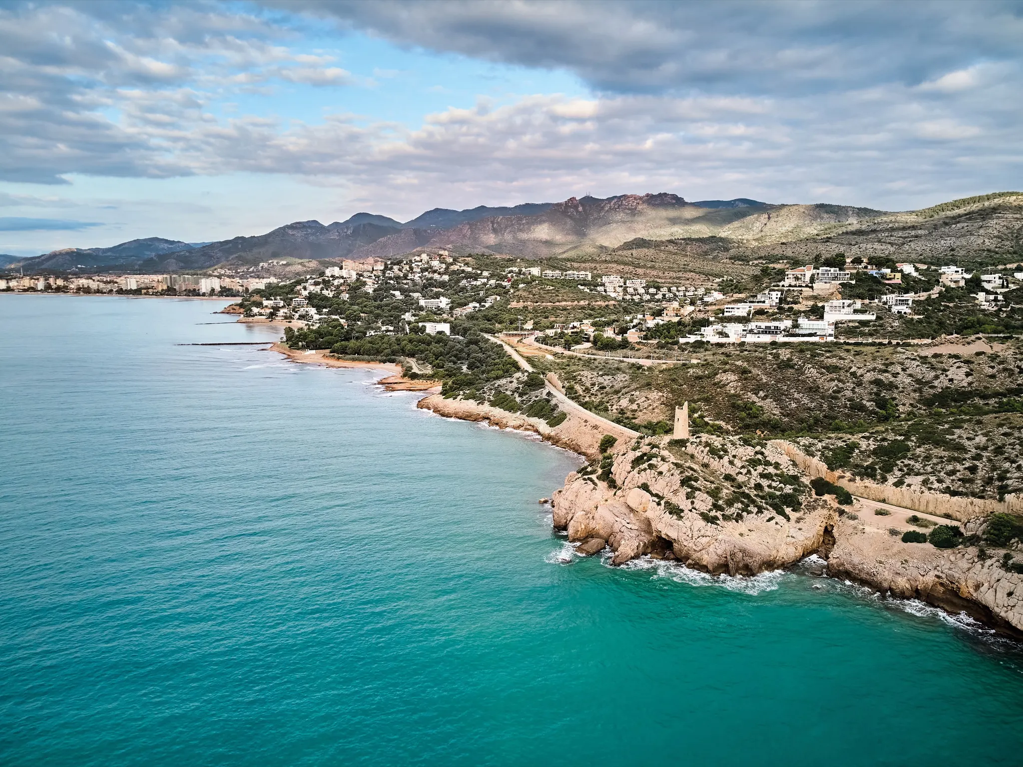 Vista aérea de la costa de La Renegà entre Benicàssim y Oropesa del Mar, con la torre vigía sobre el acantilado y el Desert de les Palmes al fondo