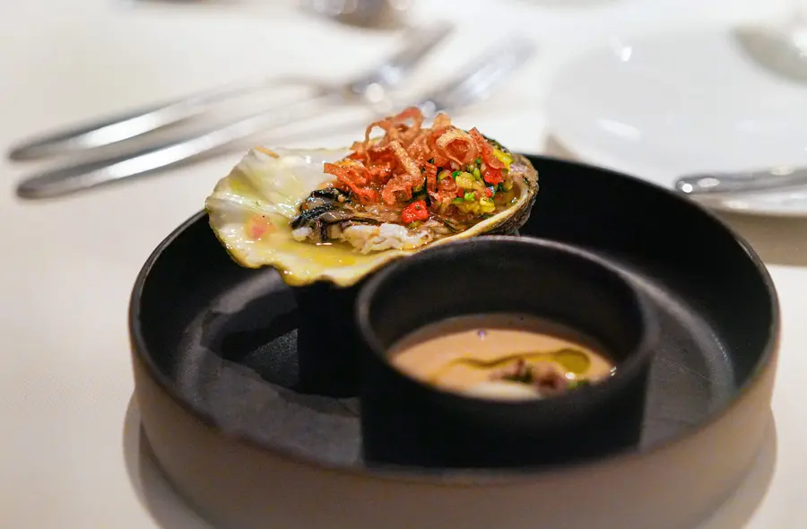 Una ostra aliñada con verduras y su caldo, servidas en un plato negro